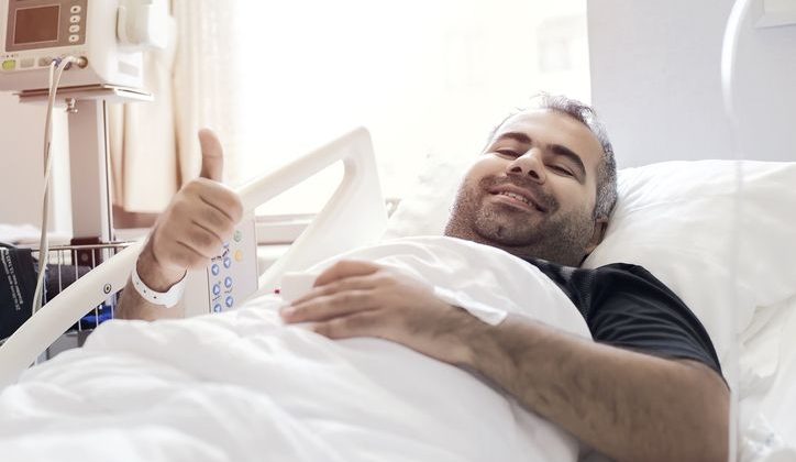 Happy hospital patient raises a thumbs up in a hospital bed