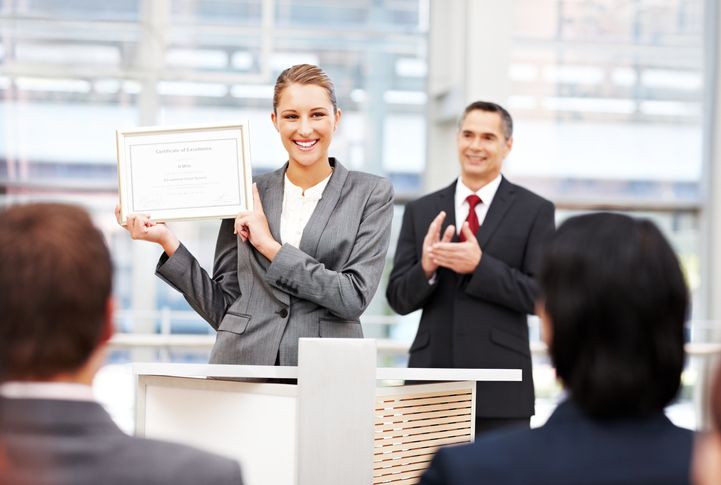 Businesswoman displays award in office in front of coworkers