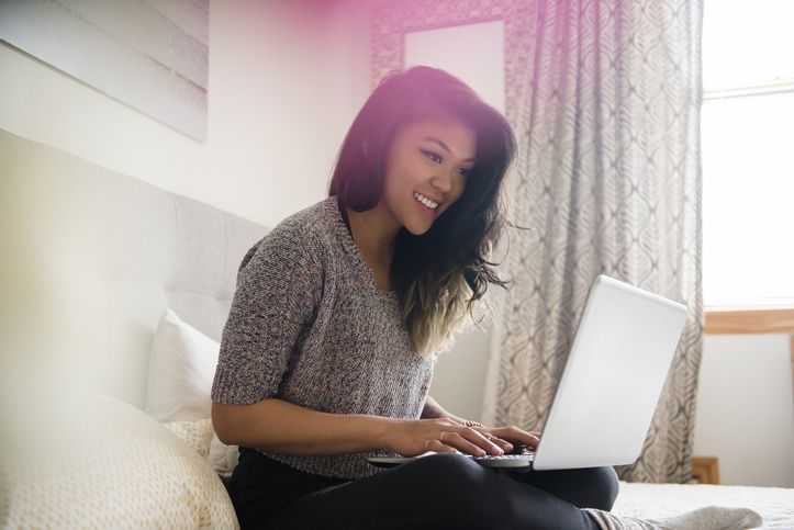 mixed race woman at home sitting on bed using laptop