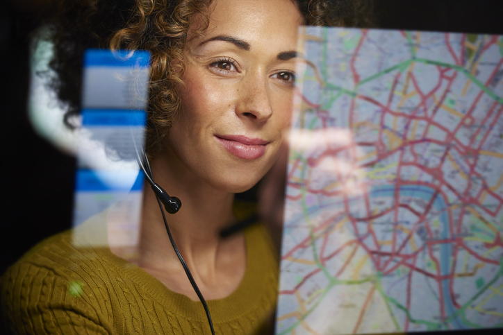 a female logistics worker is organizing dispatch of freight on her interactive digital map while talking on her headset.