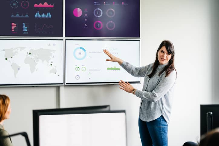 Benchmarking concept. Businesswoman explaining graphs and data displayed on large monitors in an office