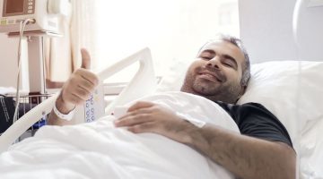 Happy hospital patient raises a thumbs up in a hospital bed