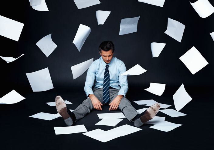 Stressed business man sitting on floor with papers falling around him.