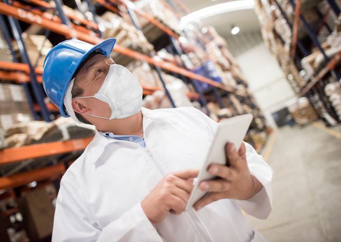 Man working at a distribution warehouse wearing a facemask to avoid COVID-19 while doing inventory